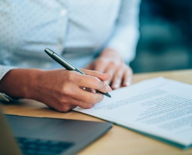 A person sitting next to a laptop signing a trust document.