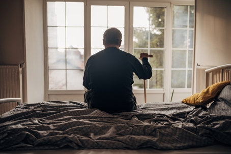 silhouette of person sitting on bed with walking cane