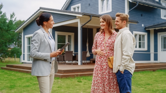 A real estate agent showing a couple a house outside