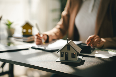 Person's hand signing a property contract on a desk with a miniature house model