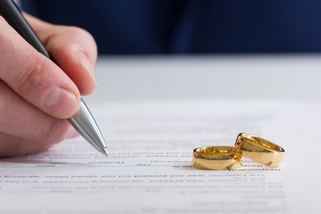 A person signing divorce papers with two wedding rings sitting on top of the papers.